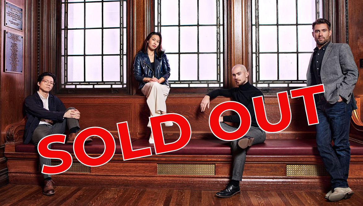Four people in a wood-paneled room pose on a bench, with a bold red SOLD OUT stamp across the image.