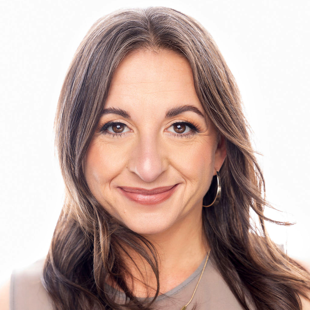 Alexis Corbin 2023 Portrait of a smiling brunette woman with hoop earrings and a beige top, against a light background.