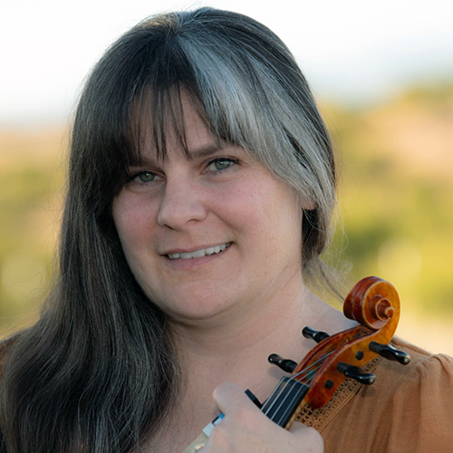 HaleyLovelace_violinsq Portrait of a woman with long dark hair holding a violin outdoors, smiling with a blurred natural background